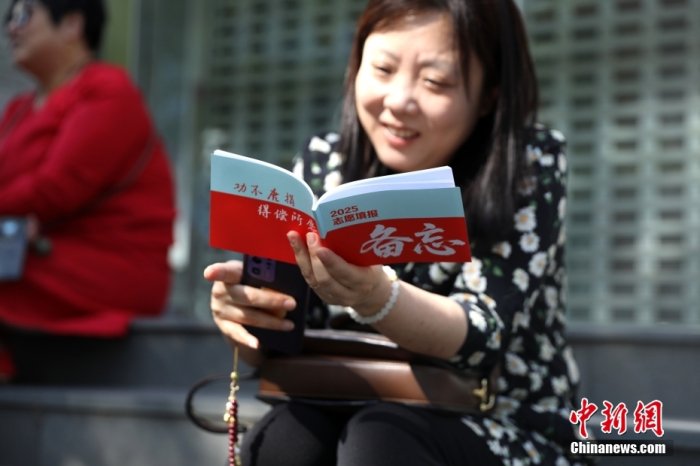 6月7日，2025年全国高考拉开帷幕。位于北京的中国人民大学附属中学考点外，家长翻阅2025志愿填报备忘资料。中新社记者 赵隽 摄